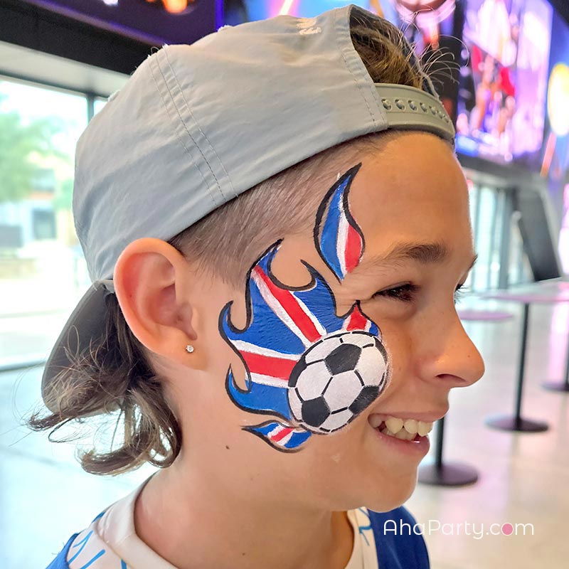 Soccer ball face painting with Union Jack colors and flame design on a child at a Dallas World Cup event